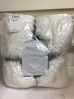 White plush throw blanket in original clear plastic packaging showing brand label and packaging details.