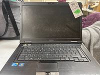 Front view of Toshiba laptop showing keyboard, touchpad, and screen. Visible dust and wear on device surfaces.