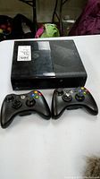Xbox 360 console with two controllers placed in front on a table, showing physical condition and included items
