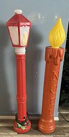 Two vintage Christmas blow molds: a red and white lantern and an orange NOEL candle with yellow flame, displayed side by side.