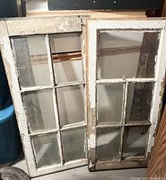 Two old wooden framed pane windows leaning upright showing peeling paint and missing/cracked glass panes