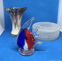 Three glass items: clear and brown fluted vase, frosted satin glass powder jar, and colorfully accented glass clown fish figurine