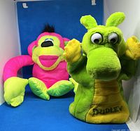 Dudley the Dragon puppet and pink monkey plush side by side on a blue background
