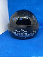 Photo of the black spherical Gemmy light projector with Haunted Mansion branding on front.