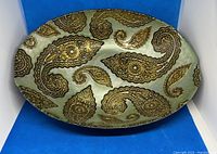 Top-down view showing the oval shape and gold paisley pattern on the iridescent glass surface.