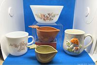 Grouped shot showing 6 white milk glass nesting bowls with gold/brown leaf pattern, two maple leaf handle ceramic measuring cups, and two decorated mugs.
