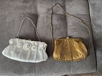 Two evening purses placed side by side on a grey fabric surface, showing the decorative design and chain straps of each purse.