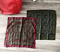 Two vintage silk scarves laid flat on a wooden floor, one olive green with paisley print and the other burgundy with intricate design.