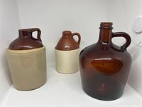 Photo showing three jugs: large amber glass jug and two ceramic jugs with brown glazed tops and beige bottoms