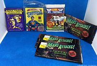 Photo showing six sealed trading card packs including NFL Football 1991, Superman movie, 1979 Star Trek movie, and three Mars Attacks! Widevision cards.