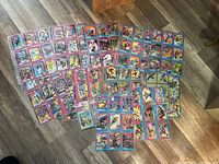 Image showing a wide spread of Marvel trading cards laid out on a floor, all in plastic sleeves. Cards are colorful with purple and red borders.