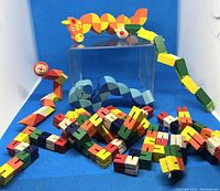 View of four wooden twist animal figures arranged on and around a clear box on blue background, and a pile of multicolored twist block strips.