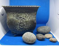 Side view of metal planter showing embossed floral design and some river rocks placed outside.