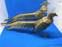 Pair of brass pheasant figures positioned side by side on blue background.