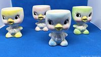 Four ceramic chick egg cups in yellow, pink, blue, and green tones shown together to illustrate the full set and colors.