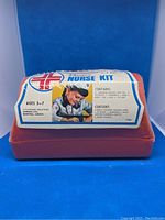 Front view showing red plastic nurse kit case with white domed lid featuring printed nurse graphics and kit title