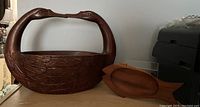 Side view of carved duck basket and wooden fish tray on table