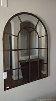 Full view of the arch-shaped metal framed mirror mounted on a wall with decorative grid-style metal bars dividing the mirror surface.