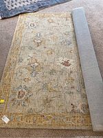 Full view of 8 x 10 floral area rug with one corner rolled showing thick grey backing, showcasing texture and color.