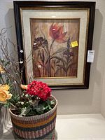 Photo of the first framed floral print and the woven basket with faux flowers to show contents of the lot