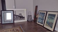 Seven-piece set including framed Asian prints, Brooklyn Bridge print, mirror, and lantern arranged on floor corner