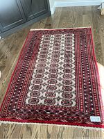 Full view of rectangular 4x6 wool carpet with cream center and red, black, beige geometric and floral design.