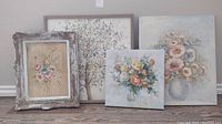 Group view of the artworks showing the signed original painting with pastel flowers in a vase, a floral print, framed floral art, and a tree print behind them on a white wall.