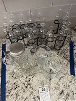 Lot showing glassware items including the metal serpentine holder with 19 glass sample/vase beakers and assorted glass tumblers and beer steins on granite countertop.