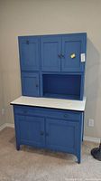 Front view of the blue painted two-piece Hoosier cabinet with upper and lower storage sections and white countertop.