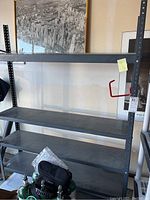 Full view of the metal shelving unit showing four shelves and one side support column with adjustment holes