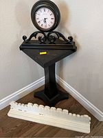 Pedestal table in black with mounted round clock and white decorative plate holder on floor