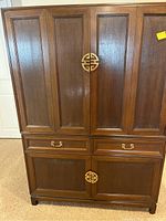 Front view of two-piece wooden cabinet with paneled doors and brass hardware