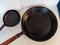 Photo showing both the large cast iron pan with a wooden detachable handle and the smaller pan with a fixed metal handle.