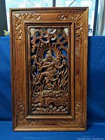 Full front view of rectangular carved wood wall art panel with ornate frame, showing deity figure and flaming motif