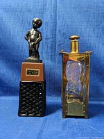 Two items on blue background: Danny Boy liquor dispenser with black textured base and statue on pedestal, beside brass-colored music box lantern with glass panels and decorative interior