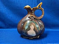 Front view of brown porcelain jug with hand painted portrait of a woman, showing overall shape and handle detail.