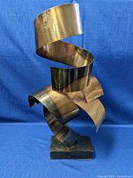 Front view of large metal sculpture on rectangular base against blue backdrop