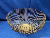 Front angle view of the metal rod art sculpture bowl on a blue fabric backdrop.