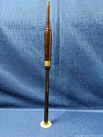 Side view of wooden snake charming flute showing full length and white mouthpiece and ring near middle