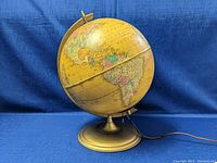 Side view of the vintage illuminated globe showing South America and part of North America with metal base and electric cord visible.