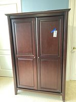 Front view of a dark brown wooden armoire cabinet with two paneled doors and round knobs.