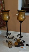Two tall metal and amber glass candle holders with three smaller candle holders on the floor between them.