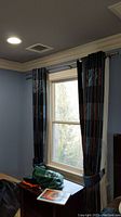 Curtain set hanging on metal rod above window, showing heavy plaid fabric pattern and tieback in blue and black hues.