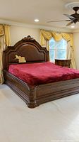 Full view of ornate king size bedframe in a bedroom with red covering on bed and carved wood frame.