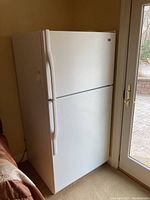 White Maytag refrigerator with top freezer, front and left side view by patio doors