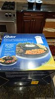 Box of Oster party serving platter with electric warming pot showing product image and features