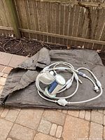 Polaris pool cleaner unit coiled with hoses on a protective cover bag outdoors.