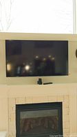 Samsung 54" TV mounted on wall above fireplace, with remote and small device on mantel below