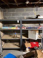 Pair of metal shelving units with adjustable wood shelves in basement setting, filled with boxes and other stored items.