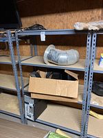 Photo showing two metal shelving units with wood shelves in a basement environment, some miscellaneous items on shelves, evidence of dirt/dust.
